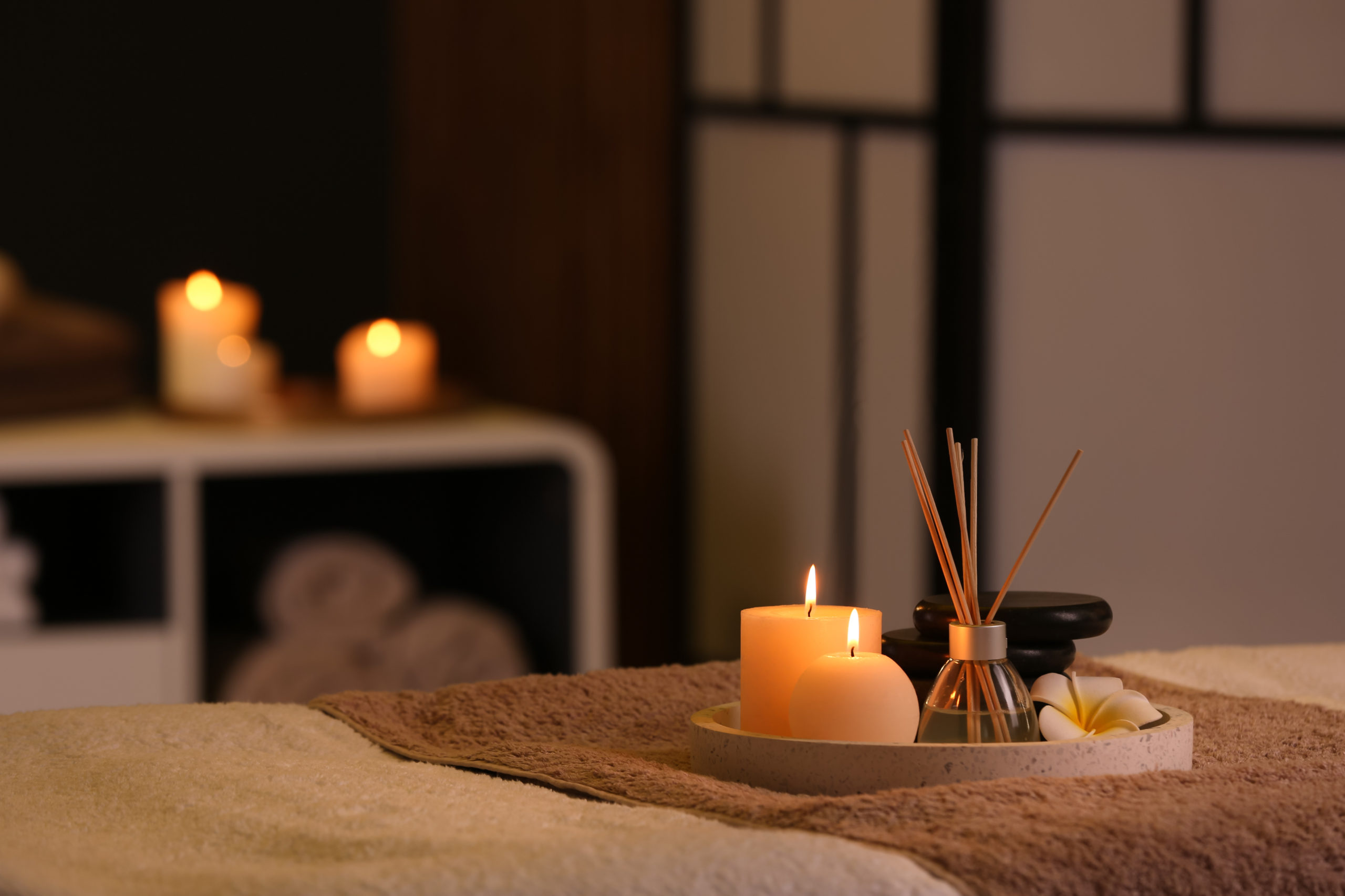 Burning candles and aromatic reed freshener on table in spa salon, space for text